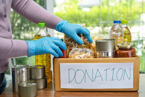 Image shows a cardboard box of donated food items, including tins and other staples.